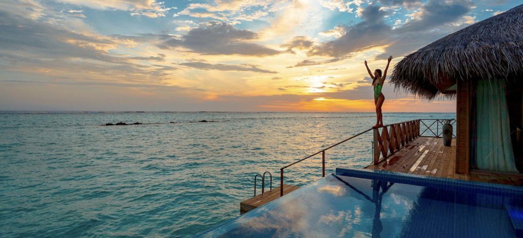 solo travel budget - woman in a hotel on the water at sunset