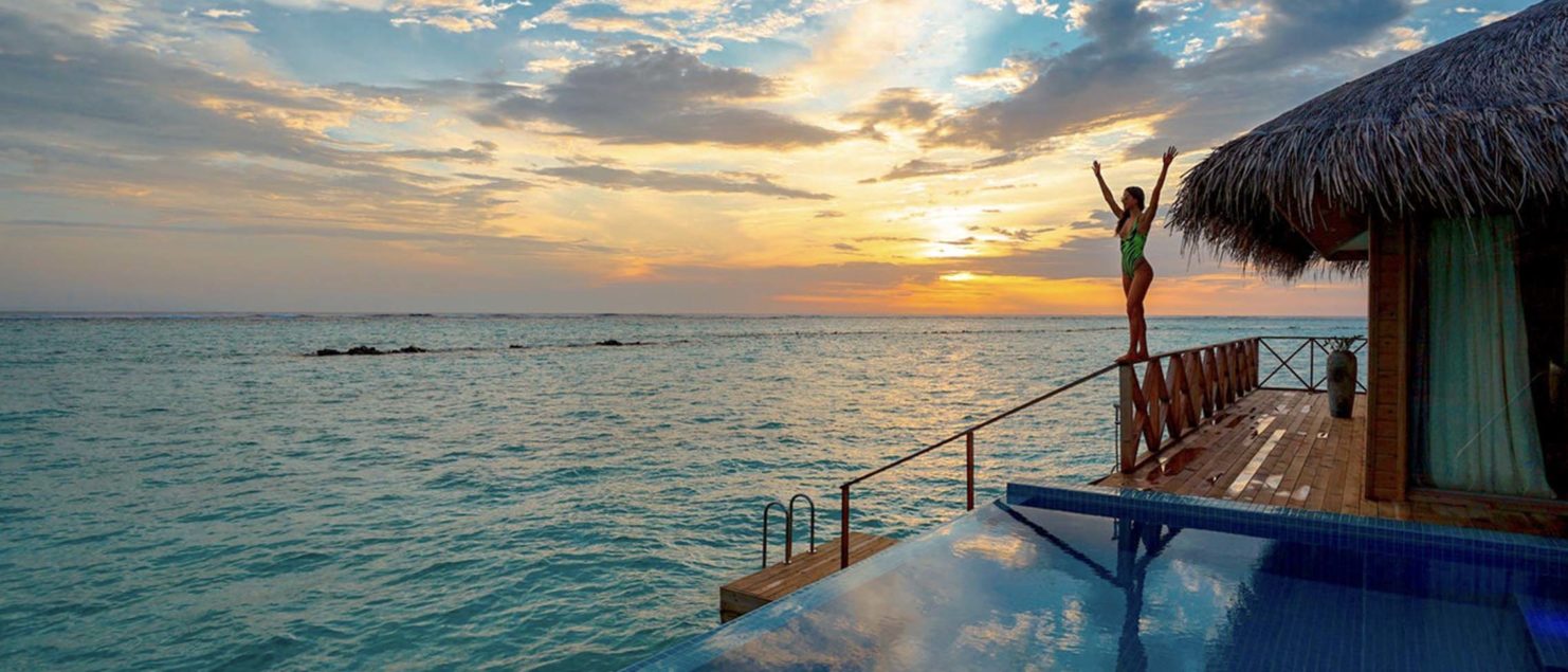 solo travel budget - woman in a hotel on the water at sunset